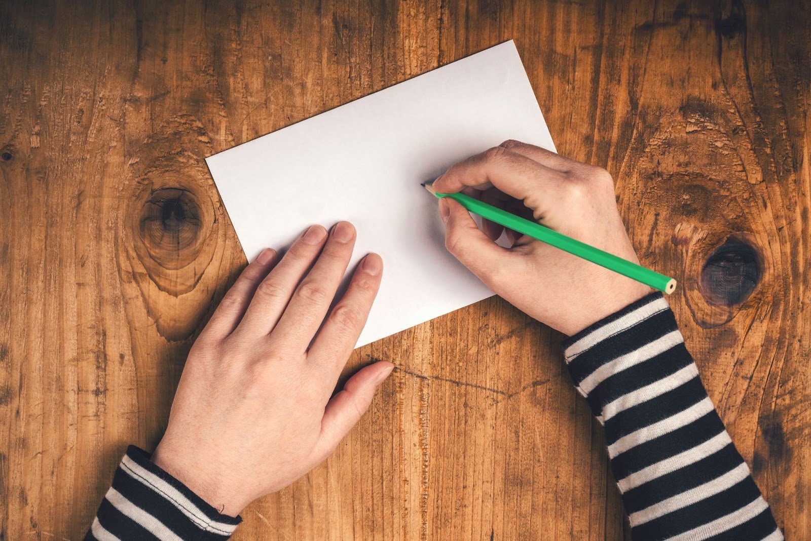 A person in a black and white shirt about to write an address on a letter after learning how to write address on letter.